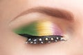 Gold, purple and green Mardi gras makeup. Woman eye with bright eyeshadows and rhinestones on false eyelashes closeup Royalty Free Stock Photo