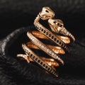 Gold ring in the form of kissing snakes with cubic zirconias and black diamonds on a leather background Royalty Free Stock Photo