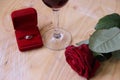 gold ring red rose and aglass of red wine on a woodenbackground.