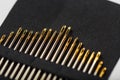 Gold sewing needles on a black background in a row
