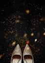 Gold shining women holiday pointy shoes on black background and shiny confetti stars around, holiday backdrop, selective focus,