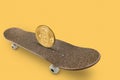 On a gold skateboard is on the edge of a big gold coin bitcoin, on a yellow background, the concept of finance and business