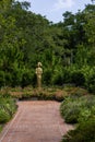 A gold statue of a woman in the garden surrounded by colorful flowers and lush green trees and plants