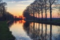 Gold sunset over river with sun rays, tree silhouettes and reflection on water