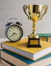 gold trophy sits on top of books next to an alarm clock