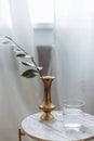 Gold vase with garnish with greens marble backsplash wooden board white drapes glass water in cozy scandinavian interior