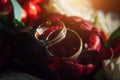Gold wedding rings on background of red flowers, selective focus, close-up. Vintage rings, reflections of light, rosebuds, macro