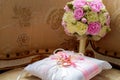 Gold wedding rings lie on a decorative silk pillow with pink satin ribbons next to the bride`s bouquet Royalty Free Stock Photo