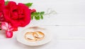 Gold wedding rings in white seashell and red rose flowers on white wooden background Royalty Free Stock Photo