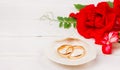 Gold wedding rings in a white seashell and red rose flowers on a white wooden background with copy space. Royalty Free Stock Photo