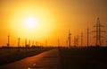 Gold wheat field, road and fiery susnet sky. High voltage electric transmission pylon silhouette tower