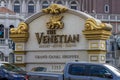 A gold and white marble sign at The Venetian hotel, resort and casino with cars and trucks driving on the street in Las Vegas
