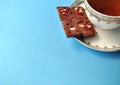 Gold and white porcelain tea cup and saucer with artisan chocolate on bright blue background with copy space Royalty Free Stock Photo