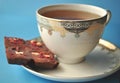 Gold and white porcelain tea cup and saucer with artisan chocolate on bright blue background with copy space Royalty Free Stock Photo