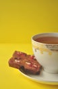 Gold and white porcelain tea cup and saucer with artisan chocolate on bright yellow background with copy space