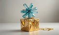 gold-wrapped gift box with blue star-shaped bow sits on white surface, accompanied by gold chain. Royalty Free Stock Photo