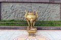 Golden amphora with incenses in front of a mural in relief depicting a battle during the Vietnam War.