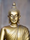 Golden antique Buddha statue. The background is light slate gray. The face of the Buddha turned to the straight