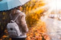 Golden autumn season. Watercolor like blurred blond girl with backpack and bright umbrella stands under rainy drops and Royalty Free Stock Photo
