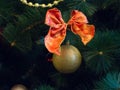 Golden ball with red ribbon bow hanging from a decorated christmas tree. New year bauble closeup foto with bright bokeh. Winter Royalty Free Stock Photo