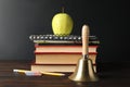 Golden bell, apple and school stationery on wooden table near blackboard Royalty Free Stock Photo