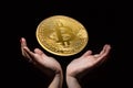 Golden bitcoin on black background over female hands. Cryptocurrency mining concept.