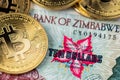 Golden Bitcoin coins new virtual money on Zimbabwe hyperinflation banknote close up image.