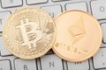 Golden bitcoin and ethereum coins on white keyboard, clipping path