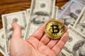 Golden bitcoin in hand against one hundred dollar bills Royalty Free Stock Photo