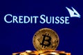 Golden bitcoin in a pile of coins on the background of Credit Suisse bank logo