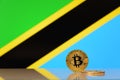 Golden bitcoin stands on a background of state flag of Tanzania