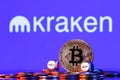 Golden bitcoin with two buy-sell cubes in a pile of coins on the background of the Kraken logo