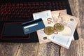 Golden bitcoins on euro banknotes and credit card on laptop keyboard suggesting bitcoin transaction or mining, wooden background