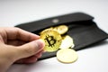 Golden bitcoins in hand. Digital symbol of a new virtual currency on white background and black wallet.