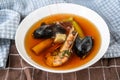 Golden broth with seafood, mussel, shrimp and vegatable in plate on towel on table