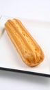 Golden brown choux pastry eclair with ridges on a white rectangular plate Royalty Free Stock Photo
