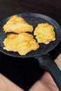 Golden-brown potato pancakes frying in a speckled non-stick pan on a hob Royalty Free Stock Photo