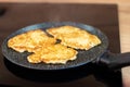 Golden-brown potato pancakes frying in a speckled non-stick pan on a hob Royalty Free Stock Photo