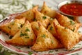 Golden Brown Samosas on a Plate with Spicy Red Dipping Sauce Garnished with Fresh Parsley