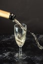 Golden champagne poured from a bottle into a glass, visible drops, bubbles and a splash