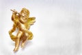 Golden cherub figure playing a flute. Figure is sparkling with wings on a white textured landscape orentated background.