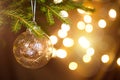 Golden Christmas ball on a live branch of a fir tree with Golden lights of garlands in defocus. New year, Christmas, holiday Royalty Free Stock Photo