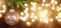 Golden Christmas ball on a live branch of a fir tree with Golden lights of garlands in defocus. New year, Christmas, holiday Royalty Free Stock Photo