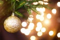 Golden Christmas ball on a live branch of a fir tree with Golden lights of garlands in defocus. New year, Christmas, holiday Royalty Free Stock Photo
