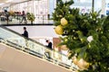 Golden Christmas balls and garland on a decorated fir tree in Shopping Mall. Blurred people on escalator, in business center make
