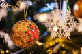 Golden christmas bauble hanging on a Christmas tree, with lights and decorations in the background Royalty Free Stock Photo