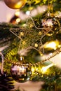 Gold Christmas star decoration hanging on a Christmas tree, with lights and bauble decorations hanging in the background Royalty Free Stock Photo