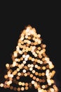 Golden Christmas tree, unfocused. Illuminated christmas tree on black background, bokeh. Glowing lights, defocused. Winter holiday Royalty Free Stock Photo