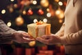 Golden Chritsmas gift with being given to person in front of Christmas tree