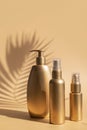 Golden clean bottles of cosmetics, sun shade from palm leaf on beige background. Cosmetic mock up bottles, tubes. Branding Royalty Free Stock Photo